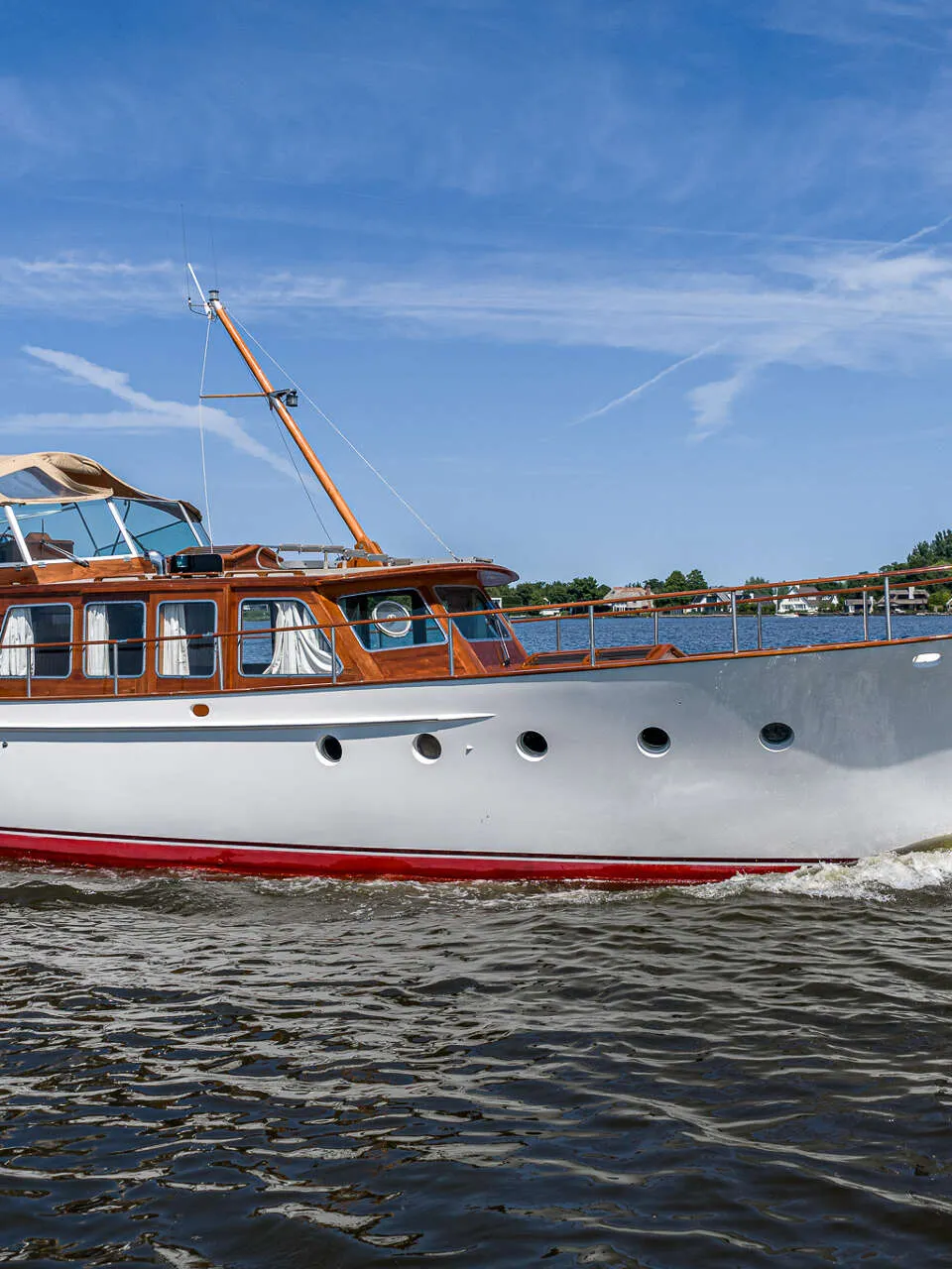 Een witte motorboot met houten opbouw en een rode streep op de romp vaart over water onder een blauwe lucht.