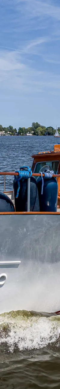 Een witte motorboot met een houten opbouw vaart op een meer onder een blauwe lucht. — Kok Spitsgatkotter 16.50