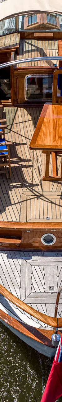 Een bovenaanzicht van een houten boot met een beige zonnescherm, varend op water, met een vlag aan de achtersteven.
