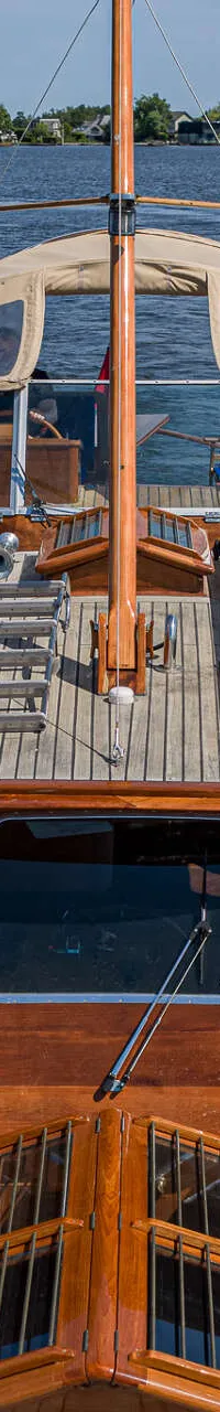 Een houten boot met een beige kap en een mast vaart op een waterweg met huizen langs de oever. — Kok Spitsgatkotter 16.50