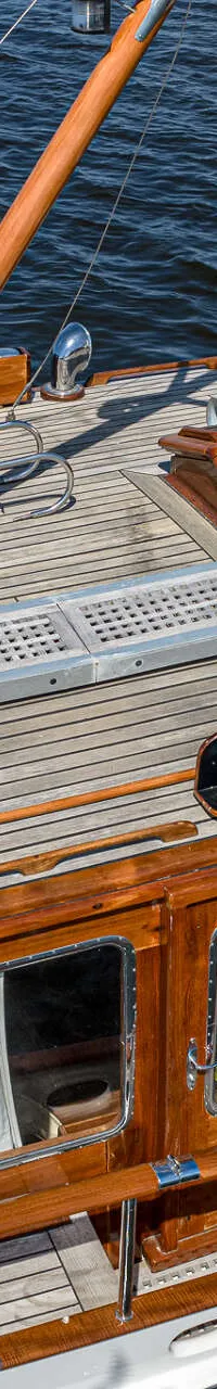 Een bovenaanzicht van een houten boot met een teakhouten dek, ramen met gordijnen en een stuurhut met beige kap.