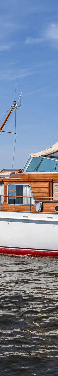 Een witte motorboot met houten opbouw en rode waterlijn vaart op een meer onder een blauwe hemel. — Kok Spitsgatkotter 16.50