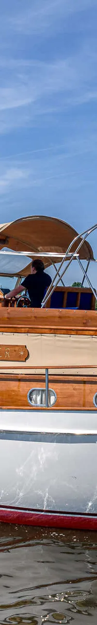 Een witte motorboot met houten opbouw en een beige bimini vaart op een meer onder een blauwe lucht.
