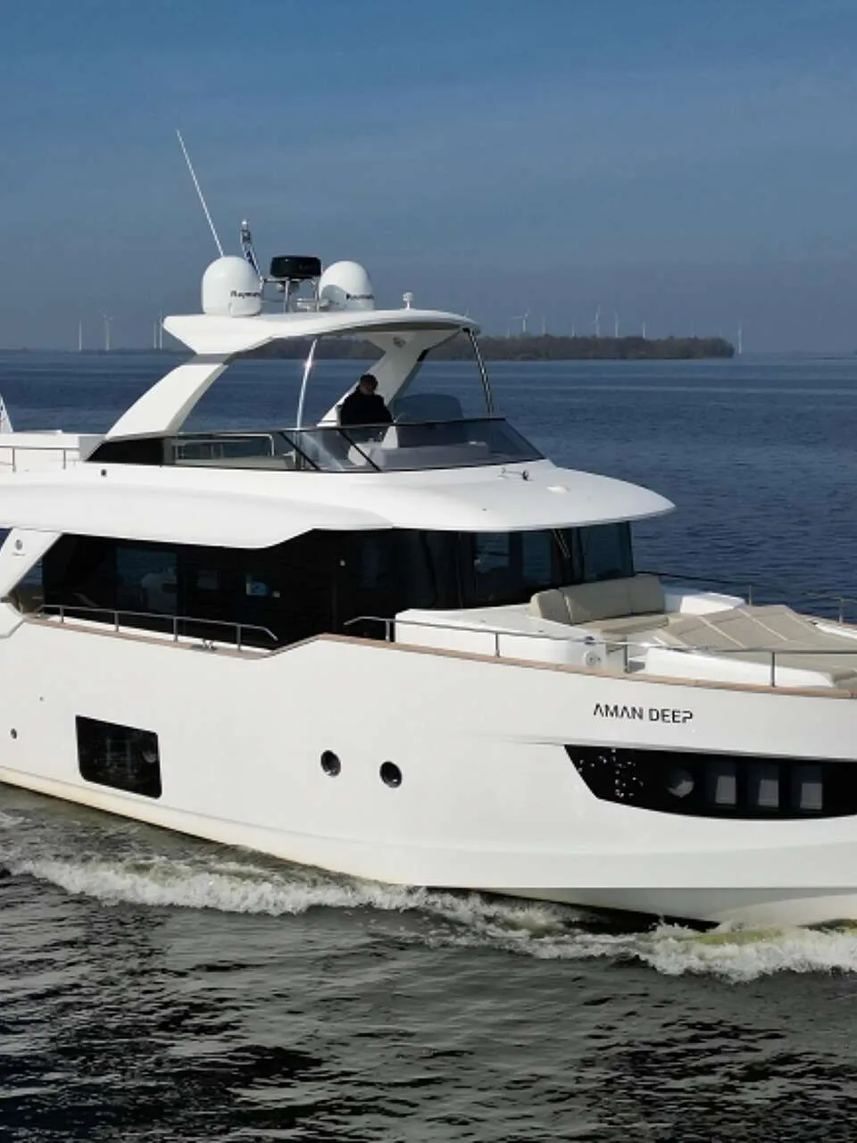 Een witte motorjacht met de naam "AMAN DEEP" vaart op open water, met een persoon aan het roer.