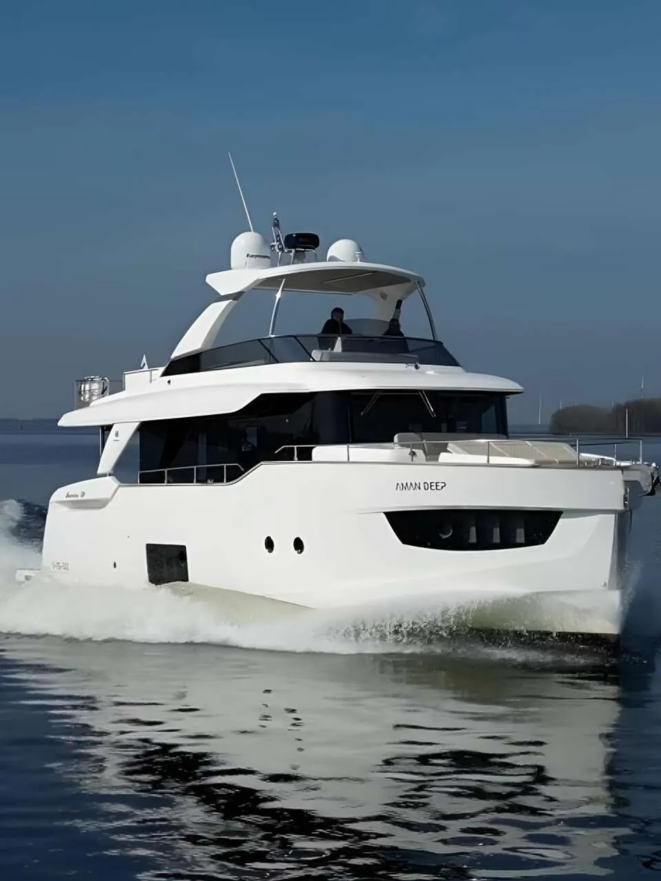 Een witte motorjacht met de naam "AMAN DEEP" vaart over rustig water, met een windmolenpark op de achtergrond.