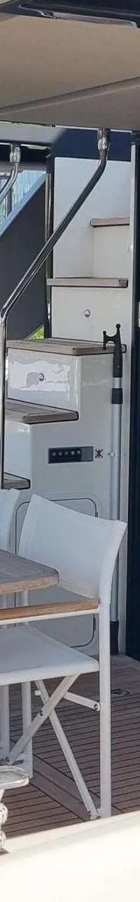 Een achterdek van een boot met een tafel, stoelen, een bank, een trap naar een hoger dek en een open toegang tot de kajuit.