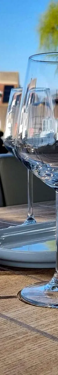 Een gedekte tafel met glazen en borden op een houten oppervlak, met een waterweg en huizen op de achtergrond.