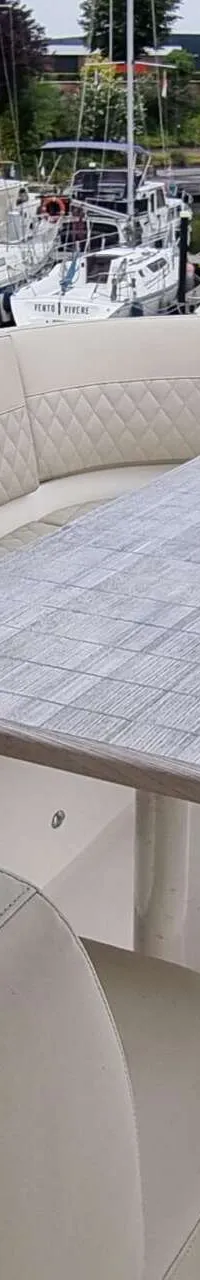 Een bootdek met een U-vormige bank en een houten tafel, met andere boten en gebouwen op de achtergrond.