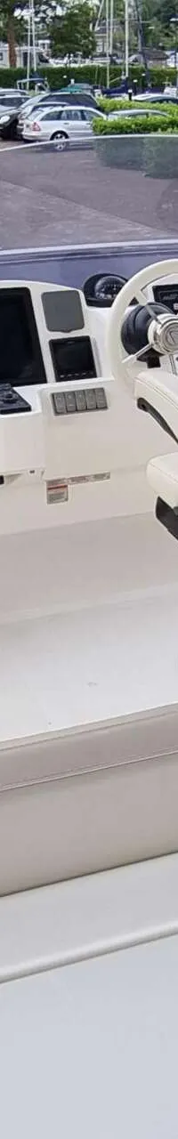 De foto toont de stuurstand van een boot met een wit stuurwiel, een beige stuurstoel en beige banken.