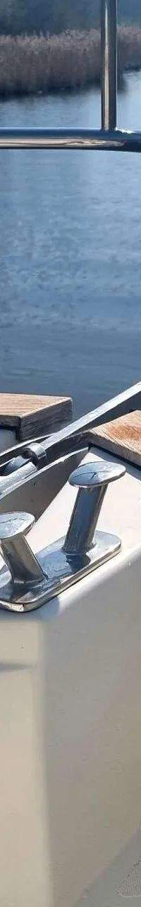 Een ankerlier met ketting en een anker op de boeg van een boot, met een reling en water op de achtergrond.