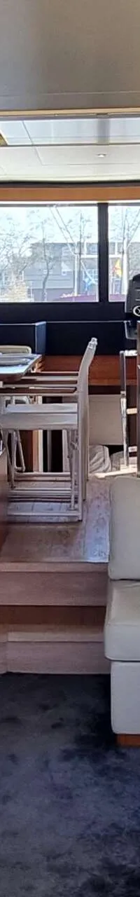 De foto toont het interieur van een boot met een zithoek, eettafel en keuken, met uitzicht naar buiten.