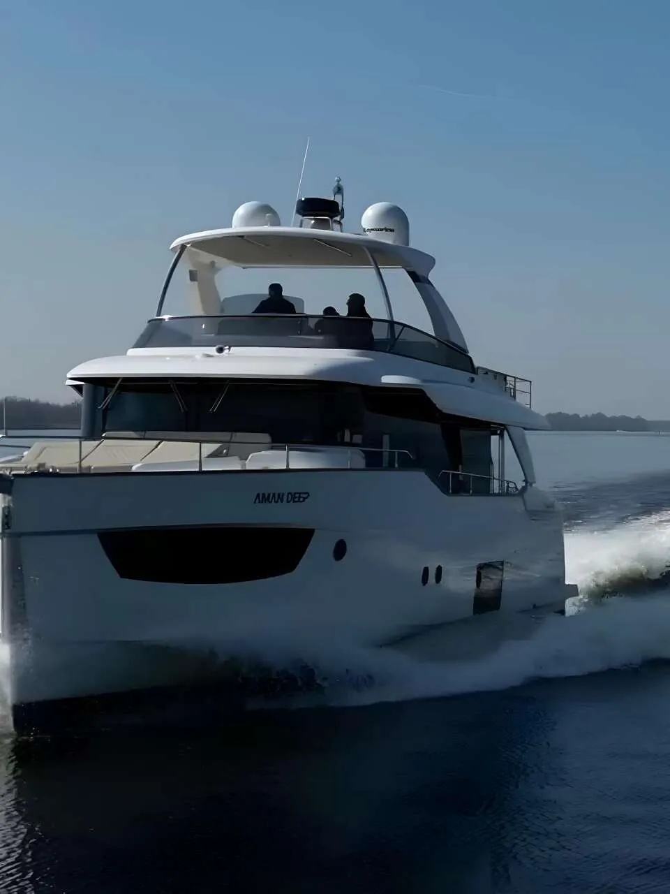 Een witte motorboot met de naam "AMAN DEEP" vaart over rustig water, met een kielzog achter zich.