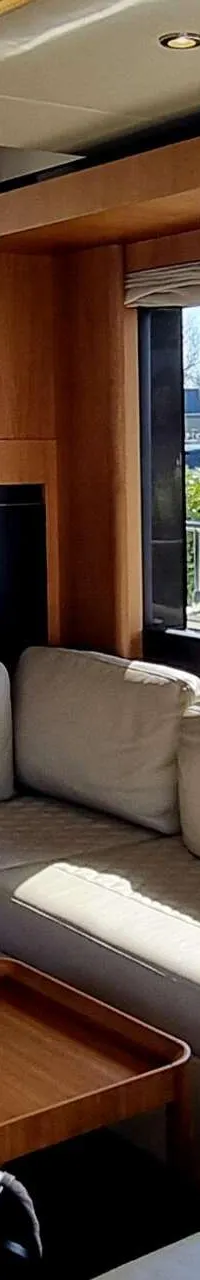 Een interieur van een boot met een beige L-vormige bank, een houten salontafel en uitzicht naar buiten.