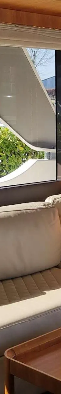 De foto toont een interieur met een beige L-vormige bank, een oranje kussen en een houten salontafel, met uitzicht naar…