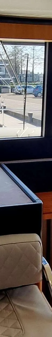 Een interieur van een boot met een stuurstand, een bankje, een tafel met tijdschriften en een uitzicht op een haven.