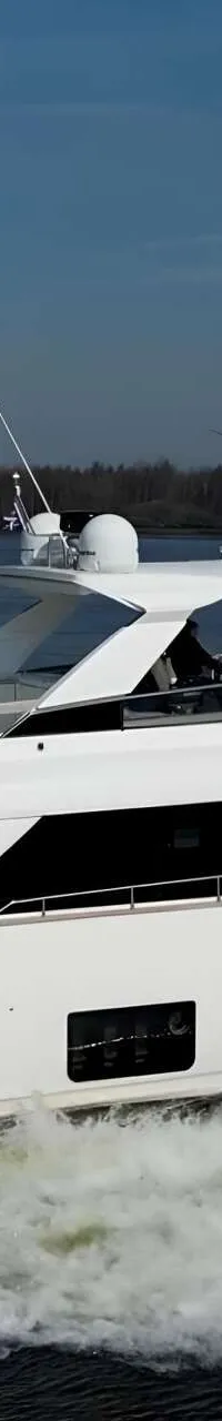 Een witte motorjacht vaart over water, met een Nederlandse vlag aan de achtersteven en windmolens op de achtergrond.
