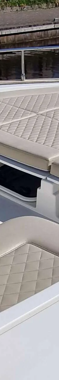 De foto toont een deel van het dek van een boot met beige gewatteerde kussens en een roestvrijstalen reling.