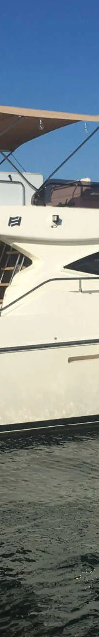 Een witte motorjacht ligt afgemeerd in een haven, met een man op de boeg en een ander op de flybridge.