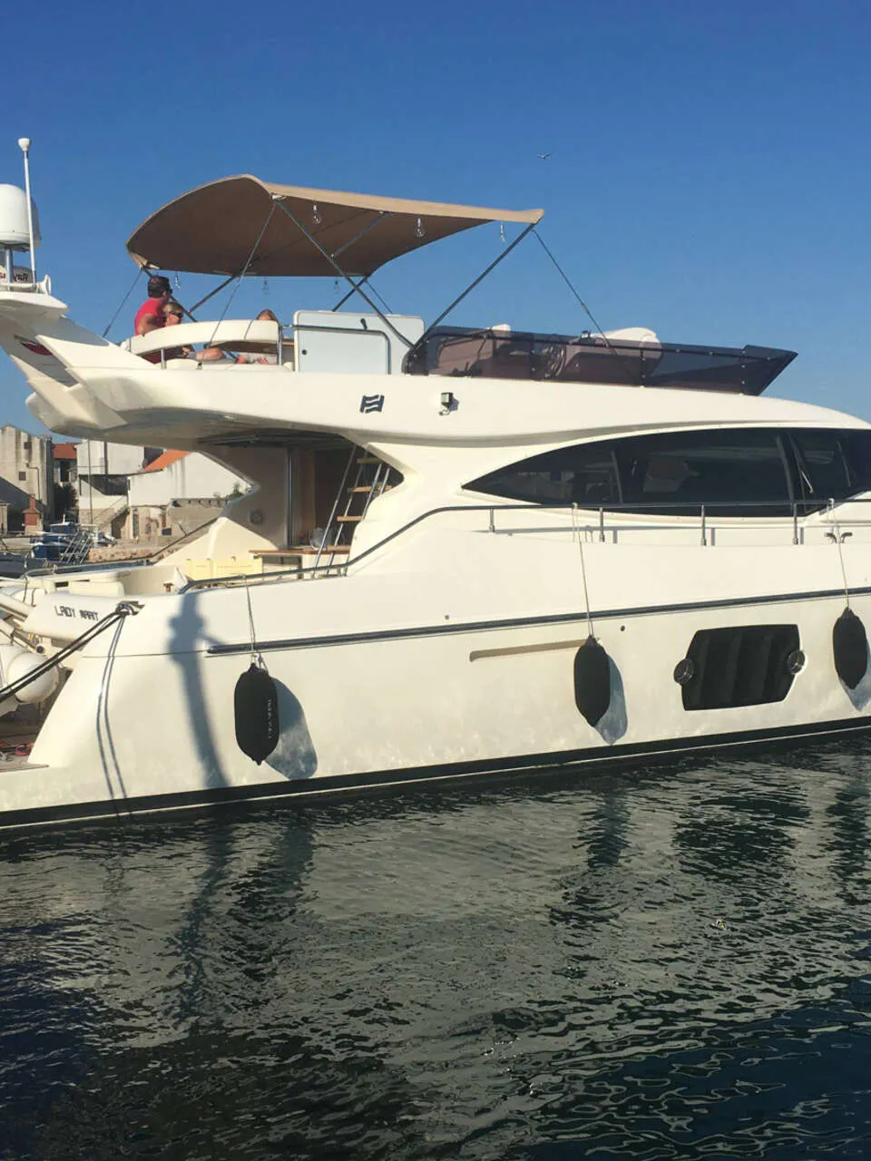 Een witte motorjacht ligt afgemeerd in een haven, met een man op de boeg en een ander op de flybridge.