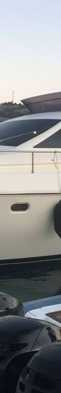 Een witte motorjacht met een bruine bimini-top ligt afgemeerd in een haven, met een kleinere boot ernaast. — Ferretti 510