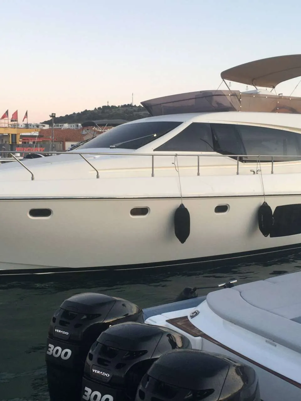 Een witte motorjacht met een bruine bimini-top ligt afgemeerd in een haven, met een kleinere boot ernaast. — Ferretti 510