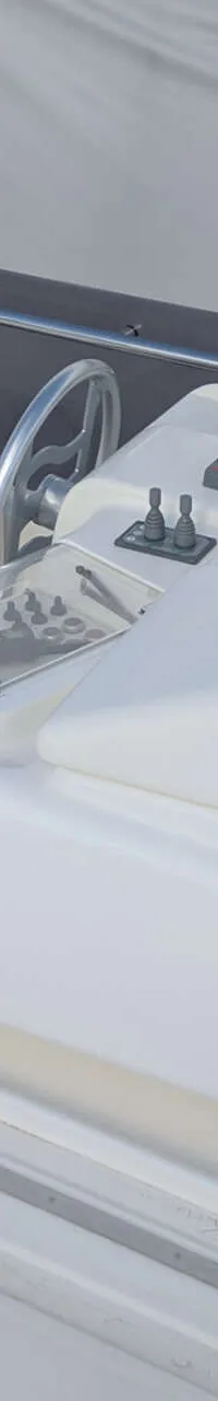 Een witte stuurstand met een stuurwiel en bedieningshendels, op een teakhouten dek.