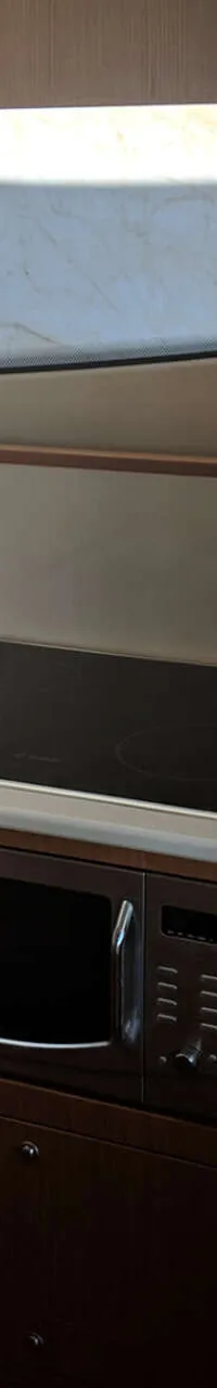 Een kombuis met een spoelbak, kookplaat, magnetron en houten kasten.