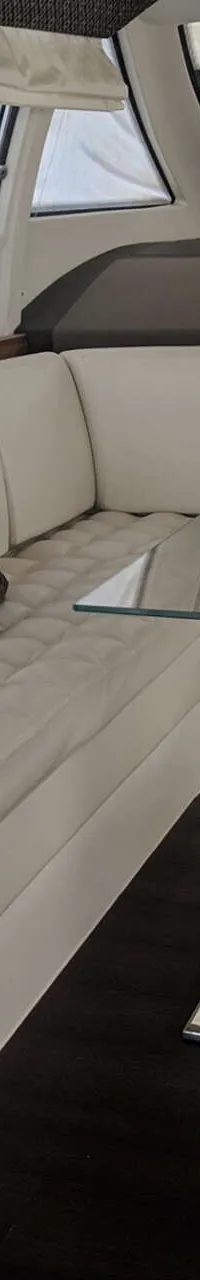 Een interieur van een boot met een witte U-vormige bank, een glazen tafel en een donkere houten vloer. — Ferretti 510
