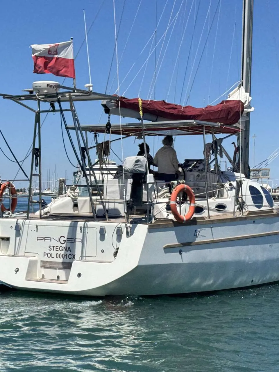 Een witte zeilboot met een Poolse vlag vaart op helderblauw water, met twee personen aan boord. — Custom Built Audax 47