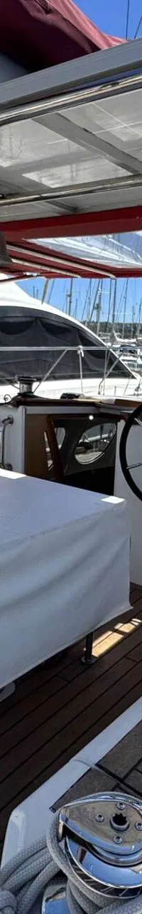 Een dek van een zeilboot met een stuurwiel, een tafel met witte hoes, en een luifel met zonnepanelen. — Custom Built Audax 47