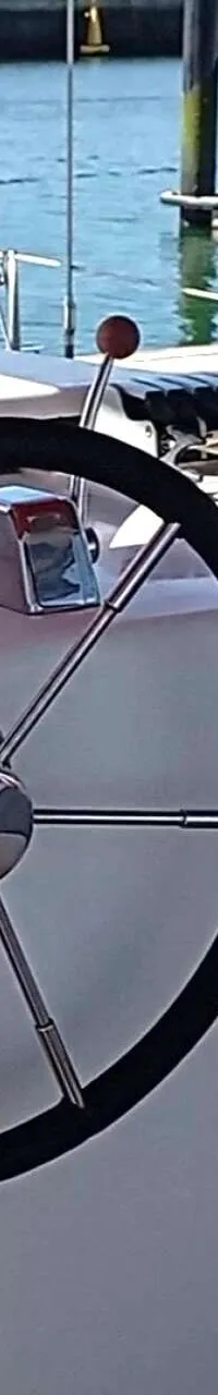 Een stuurwiel met zes spaken en een zwart handvat op een wit dashboard met een lier en een hendel.