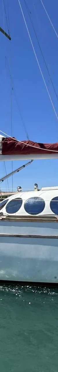 Een witte zeilboot met rode zeilen en een reddingsboei aan de achterkant ligt in het water. — Custom Built Audax 47