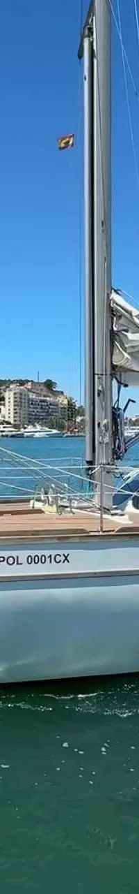 Een witte zeilboot met de naam "PANGEA POL 0001CX" vaart op turquoise water onder een heldere blauwe lucht.