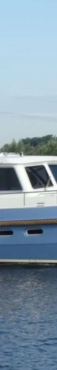 Een blauw-witte motorboot met de naam "Nika" vaart op rustig water, met een Nederlandse vlag aan de achtersteven.