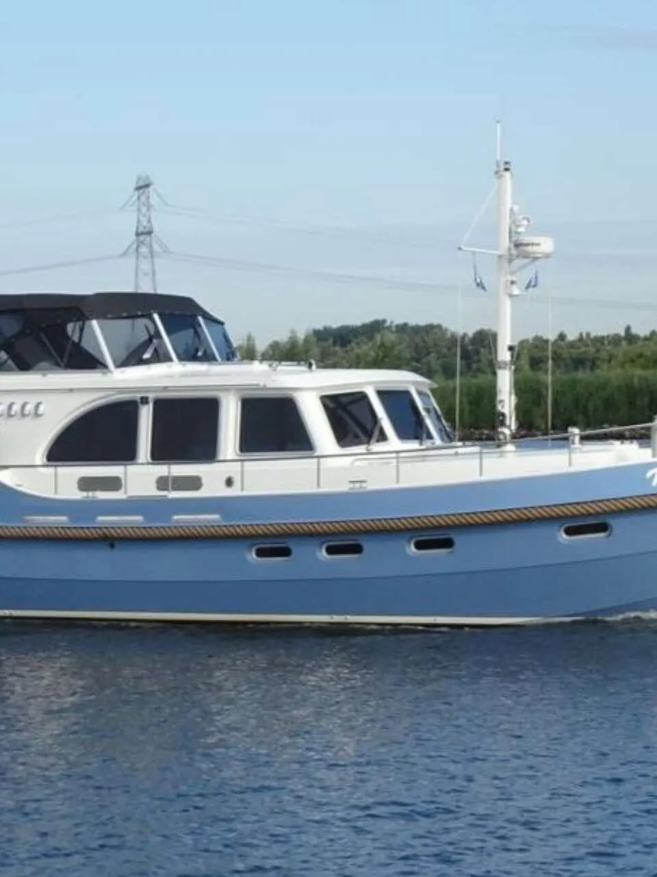 Een blauw-witte motorboot met de naam "Nika" vaart op rustig water, met een Nederlandse vlag aan de achtersteven.