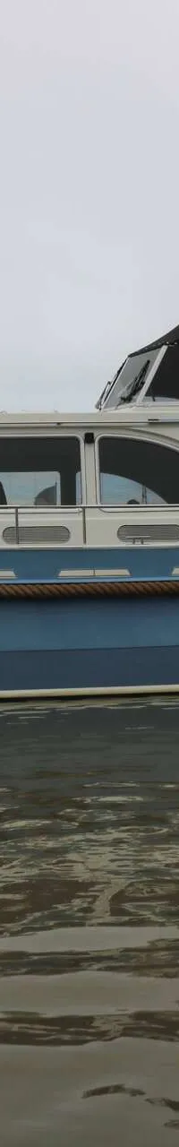 Een blauw-witte motorboot met de naam "Neba" ligt aan een steiger onder een bewolkte hemel. — Boarncruiser 50 Classic Line