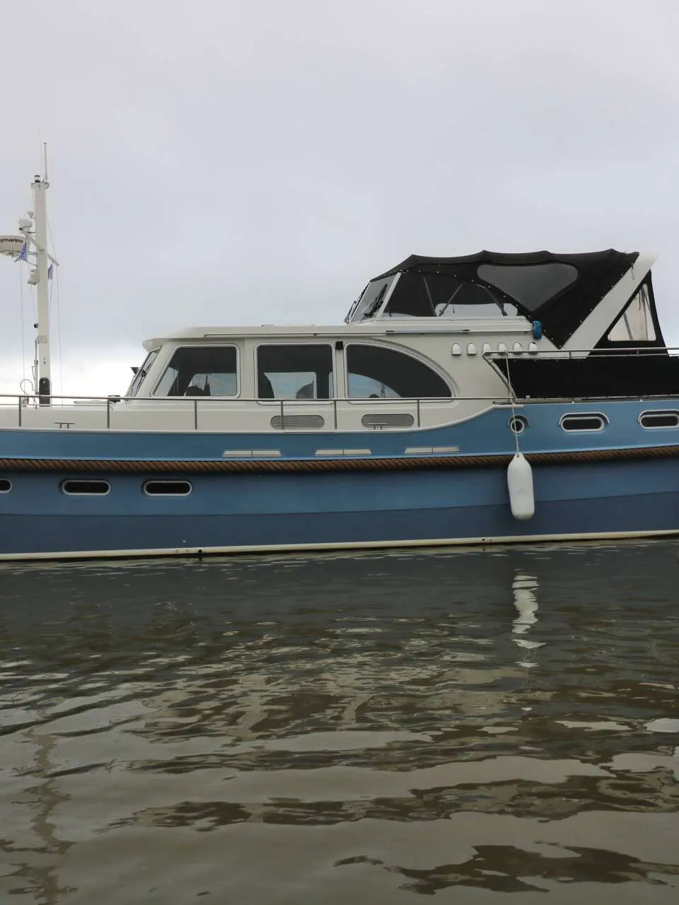 Een blauw-witte motorboot met de naam "Neba" ligt aan een steiger onder een bewolkte hemel. — Boarncruiser 50 Classic Line