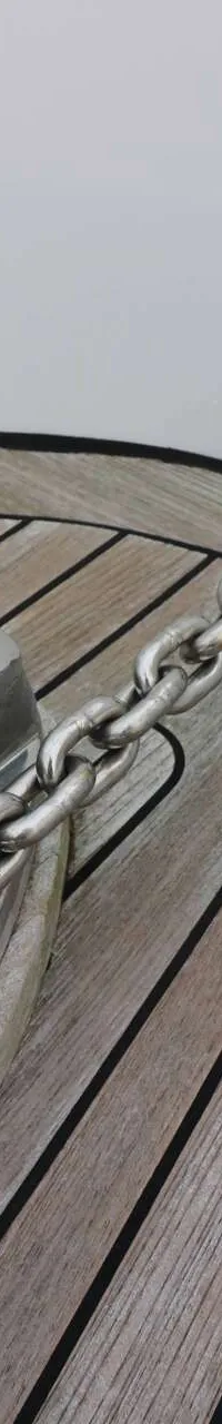 Een detailfoto van een ankerlier met ketting op een houten dek.