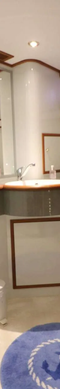 Een badkamer op een boot met een toilet, wastafel, spiegel, douchecabine en een blauw vloerkleed met een anker.