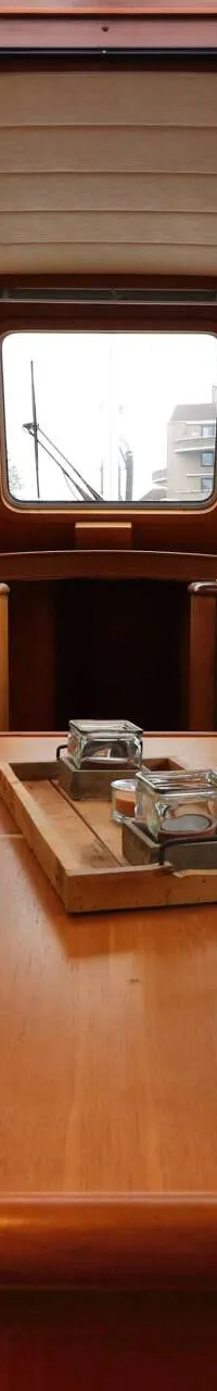 Een interieur van een boot met een houten tafel, blauwe banken, een stuurwiel en een scheepsmodel.