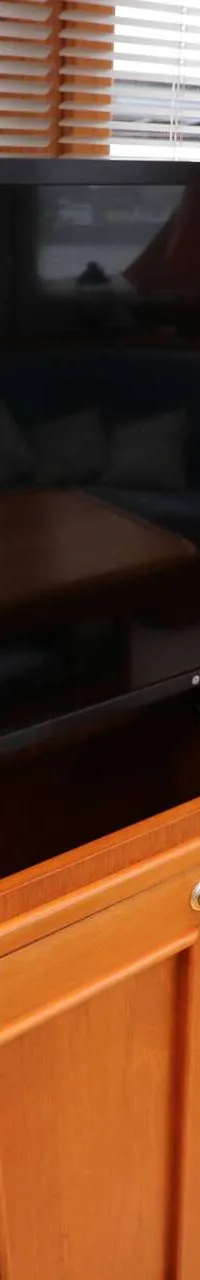 Een LG-televisie staat op een houten kast met twee deuren, naast een beige fauteuil en een champagnekoeler.