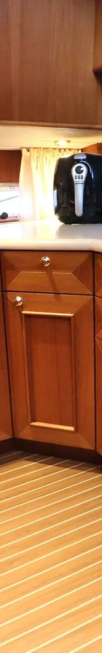 Een hoekkeuken met houten kasten, een aanrechtblad met spoelbak en kookplaat, en een gestreepte houten vloer.