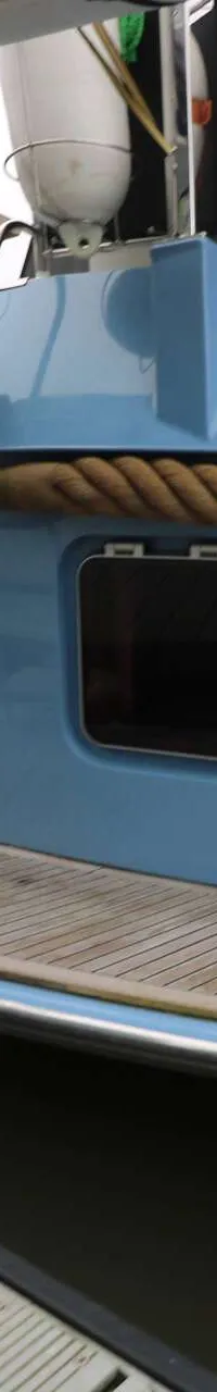De achterkant van een lichtblauwe boot met een zwemplateau en een trapje, afgemeerd aan een steiger.