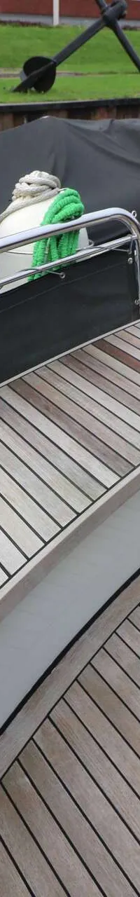 Een teakhouten dek met twee houten banken, een reling en een zwarte afdekking.