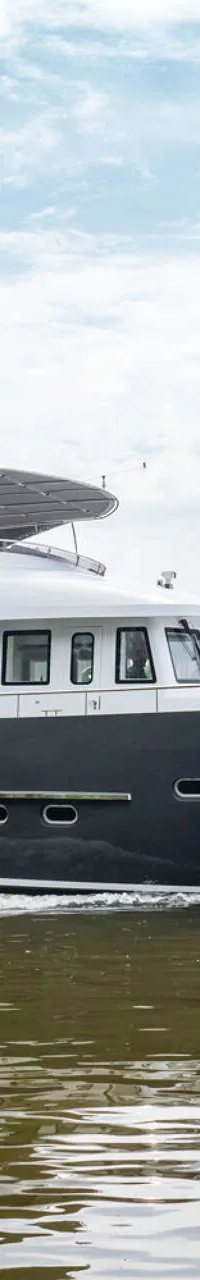 Een donkergrijze motorboot met een witte opbouw vaart over rustig water onder een bewolkte hemel. — Bloemsma Trawler 70