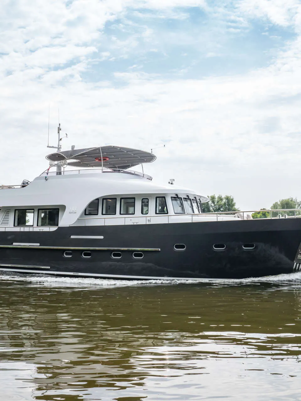 Een donkergrijze motorboot met een witte opbouw vaart over rustig water onder een bewolkte hemel. — Bloemsma Trawler 70
