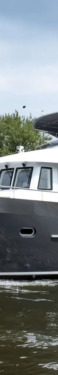 Een donkergrijze motorboot met een witte opbouw vaart over water, met een De Valk Yacht Brokers-logo rechtsboven.