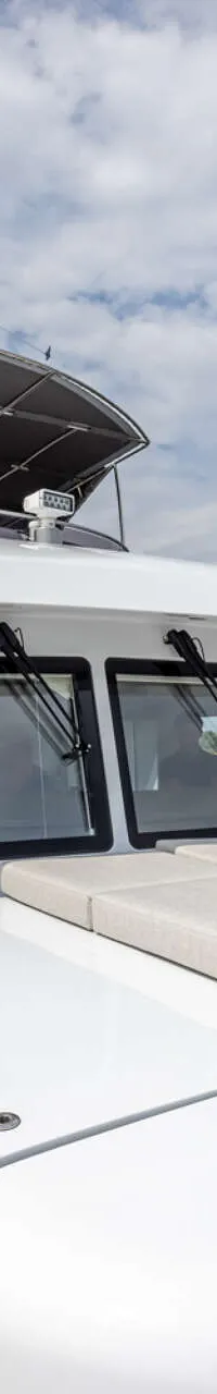 Een witte motorboot met een houten dek en een zonnedek met kussens vaart op een rivier onder een bewolkte hemel.