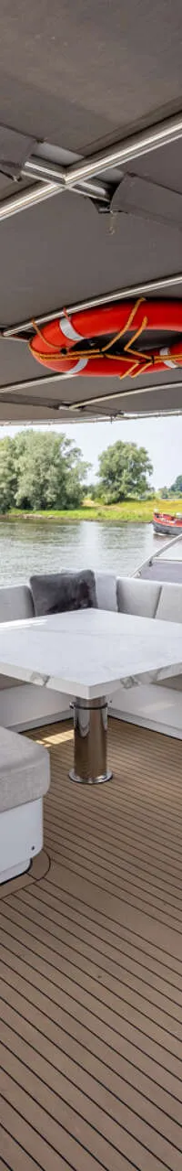 De foto toont het achterdek van een jacht met een zithoek, een stuurstoel en een bijboot, varend op een rivier.
