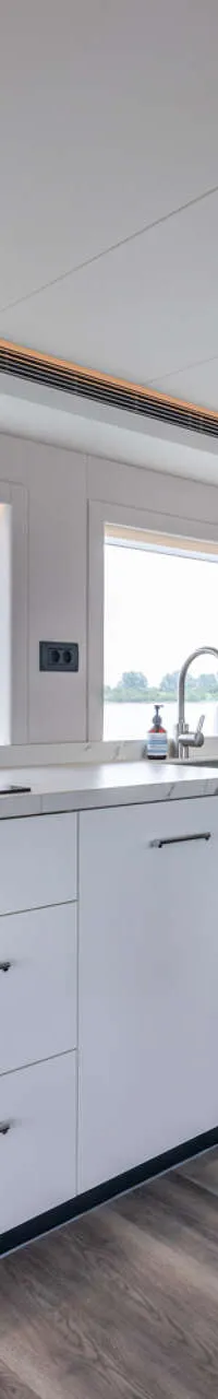 Een moderne kombuis met witte kasten, een marmerlook aanrechtblad, een kookplaat, spoelbak, oven en uitzicht op water.
